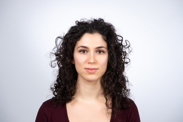 Attractive young brown haired woman looking at camera. Portrait of caucasian curly haired female....