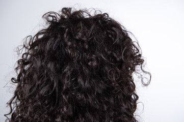 Brunette Women's curly hair rearview. Closeup of glossy wavy dark hair. Hair texture. White...