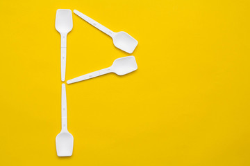 White plastic spoons in the form of letter P on yellow background. Top view. Copy, empty space for text