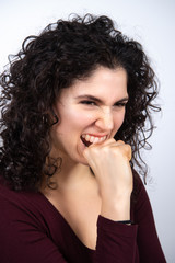 Angry young woman biting her fist. Isolated on white background. Excited brunette expresing her emotions. Human emotion concept.