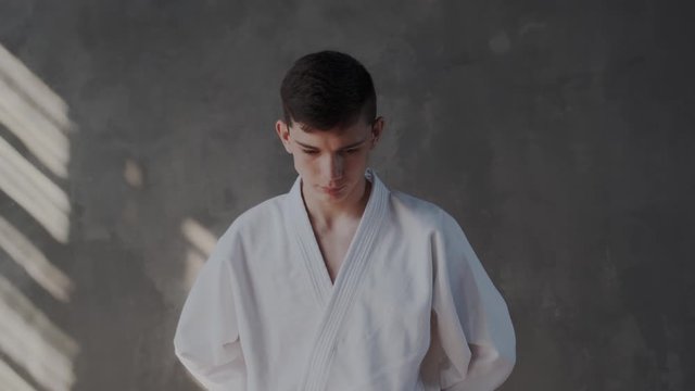 Handsome guy raises head and makes a welcome gesture. He puts his hands together and bows while looking at the camera. Respect sight in lens. Taekwondo traditional martial arts