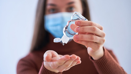 Woman in protective mask applying an antibacterial antiseptic gel for hands disinfection from...