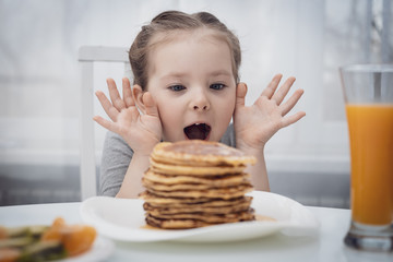 Selected focus. Little kid looking at homemade pancakes with honey on table