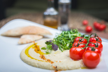 Traditional appetizer hummus with bread cakes, pita, on a plate with vegetables and sauce.