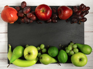 fruits background green and red color set on dark stone slake plate and white wood table. Summer abstract creative trendy fresh health concept. Flat lay top view copy space.