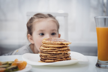 Selected focus. Little kid looking at homemade pancakes with honey on table