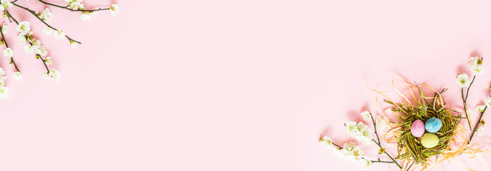 Stylish background with colorful easter eggs isolated on pink pastel background with blooming cherry branches. Horizontal long banner for web design. Flat lay, top view, mockup, overhead, template.