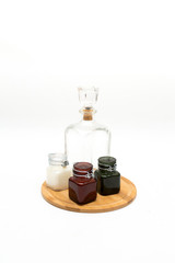 Vintage glass decanter made of transparent glass without a pattern and three colored glass jars on  a wooden round stand on a white background