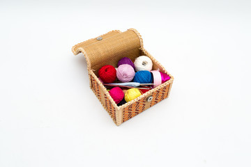 A box with multicolored reels of thread and hooks for home knitting. Still life on a white background