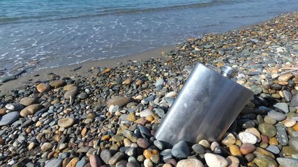 vintage metal hip flask on pebbles on a beach. celebration of men's holiday at sea. conception International Men's Day and Fatherland defender day February 23. copy space