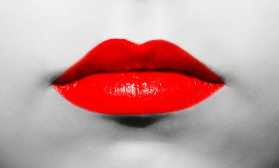 Female lips close-up with red lipstick of bright juicy vibrant color on a background of black and white face.