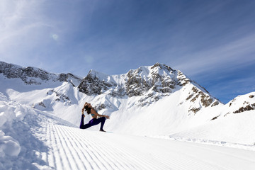 Fototapeta na wymiar A young woman practice yoga in mountains. With a great view of snow and winter landscape.
