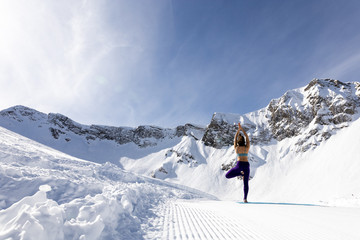 A young woman practice yoga in mountains. With a great view of snow and winter landscape.