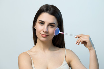 Close-up of a young girl in a light top on a white background making a facial make-up. A pretty...