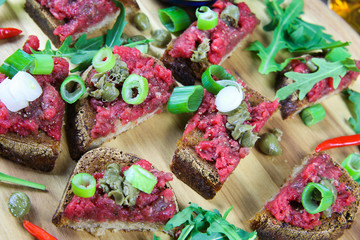 Hearty hefty german snack: isolated wood plate with roasted beef tatar garlic bread, spring onions, capers and rucola salad leaves