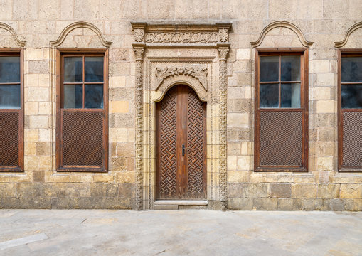 Facade of old abandoned stone decorated bricks wall with arched wooden door and four wooden shutter windows 