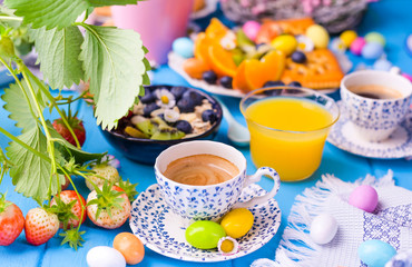 Easter breakfast. Fresh aromatic espresso coffee and easter colored eggs on a blue wooden background. Muesli, strawberries for breakfast.