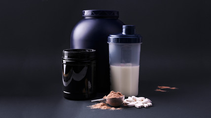 Sports nutrition supplements on a black background. Fitness, bodybuilding, healthy lifestyle concept. Whey protein powder in measuring scoop. Copy space