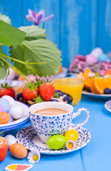Easter breakfast. Fresh aromatic espresso coffee, orange juice, easter colored eggs, granola, on a blue wooden background. Copy space