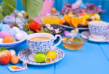 Easter breakfast. Fresh aromatic espresso coffee, orange juice, easter colored eggs, granola, honey on a blue wooden background. Copy space