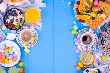 Easter breakfast flat lay. Espresso coffee, cake with jam, cookies, fresh orange juice, fruits, granola, honey, strawberries with leaves and berries . Colored eggs for Easter Sunday. Copy space