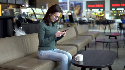 Fototapeta na wymiar A young woman is sitting in a cafe with a phone. The girl is in correspondence on a smartphone. Close-up.