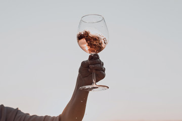 Glass of wine with splashes in woman's hand against the sunset sky. - Powered by Adobe