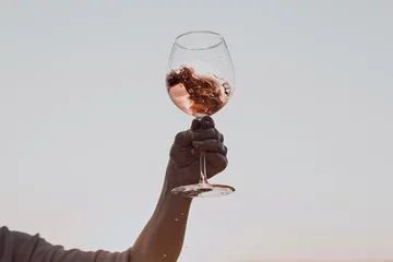Zelfklevend Fotobehang Glass of wine with splashes in woman's hand against the sunset sky. © Ira_Shpiller