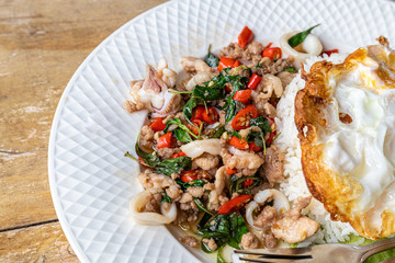 Stir fried squid basil and minced pork with steamed rice and fried egg on a white plate.