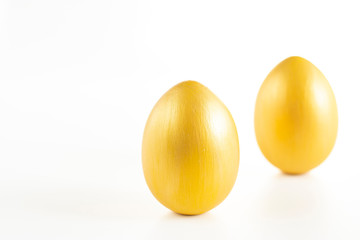 Two eggs of gold color on a white background. Minimalistic composition. Easter holiday card. Creative copy space.