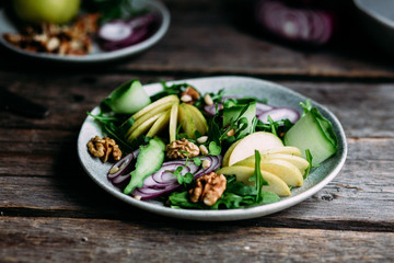 Vegetarian salad of fresh apples with arugula, onions and nuts in a plate on the table