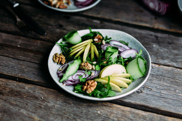 Vegetarian salad of fresh apples with arugula, onions and nuts in a plate on the table
