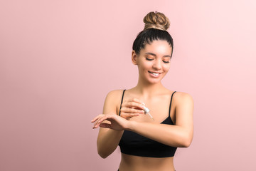 beauty woman with gathered hair applying body oil moisturizer against a pink background