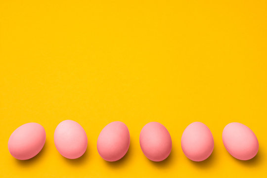 easter yellow background with a row of pink colored eggs with copy space on top