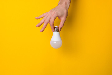 closeup hand holding white led lighting bulb against a yellow wide background banner with...