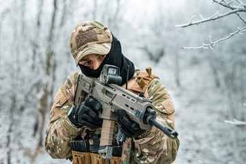 Airsoft man in camouflage uniform and machinegun with optical sight. Soldier in the winter forest....