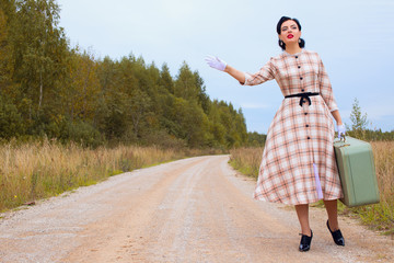 Woman in retro clothes of the 1920s. Beautiful girl stands on the road with a suitcase. Clothing in...