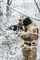Airsoft man in camouflage uniform and machinegun with optical sight. Soldier in the winter forest....