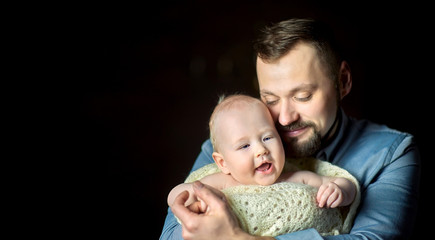 A happy father lives in the arms of a newborn baby, hugs and poses creamly. Paternity