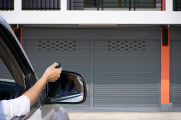 Woman in car, hand holding and using remote control to open the automatic shutter roller steel...