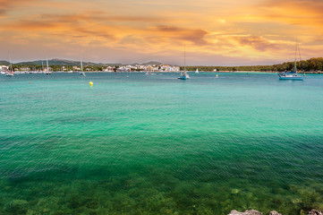 Mediterranean port in the south east of Mallorca, Spain. Clear emerald green waters and orange sky. Fishing village in the background. 