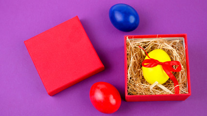 Easter celebration. A yellow Easter egg tied with a red ribbon lies in a red gift box on a yellow background. Easter background