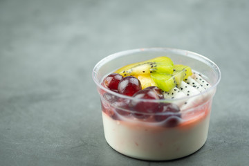 Plastic bowl yogurt smoothie with fresh fruits, Kiwi, grape and dragon fruit slice.