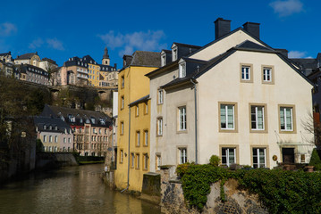 Fototapeta na wymiar Blue sky view of beautiful medieval pastel colorful houses on the river in Luxembourg City Grund (lower city) neighborhood with the upper city in the background
