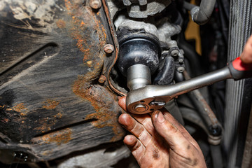 The car mechanic unscrews the diesel filter next to the oil pan with a metal wrench, visible man hands.