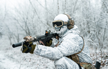 Airsoft man in white camouflage uniform with machinegun. Soldier with muchinegun stood on knelt in...