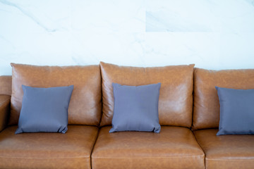Gray color pillow on brown sofa of white wall.