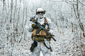 Military man in white camouflage uniform with machinegun. Soldier in the winter forest territory background. Horizontal photo.