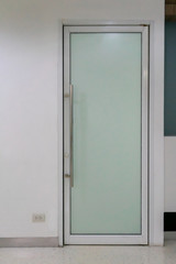 Narrow and tall glass door on white wall. Interior design detail