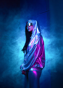 Neon Portrait Of A Girl Of Asian Appearance, Dressed In Futuristic Clothes And Glasses. Neon Blue And Pink Light. Virtual Reality Glasses And Binary Code In Them.